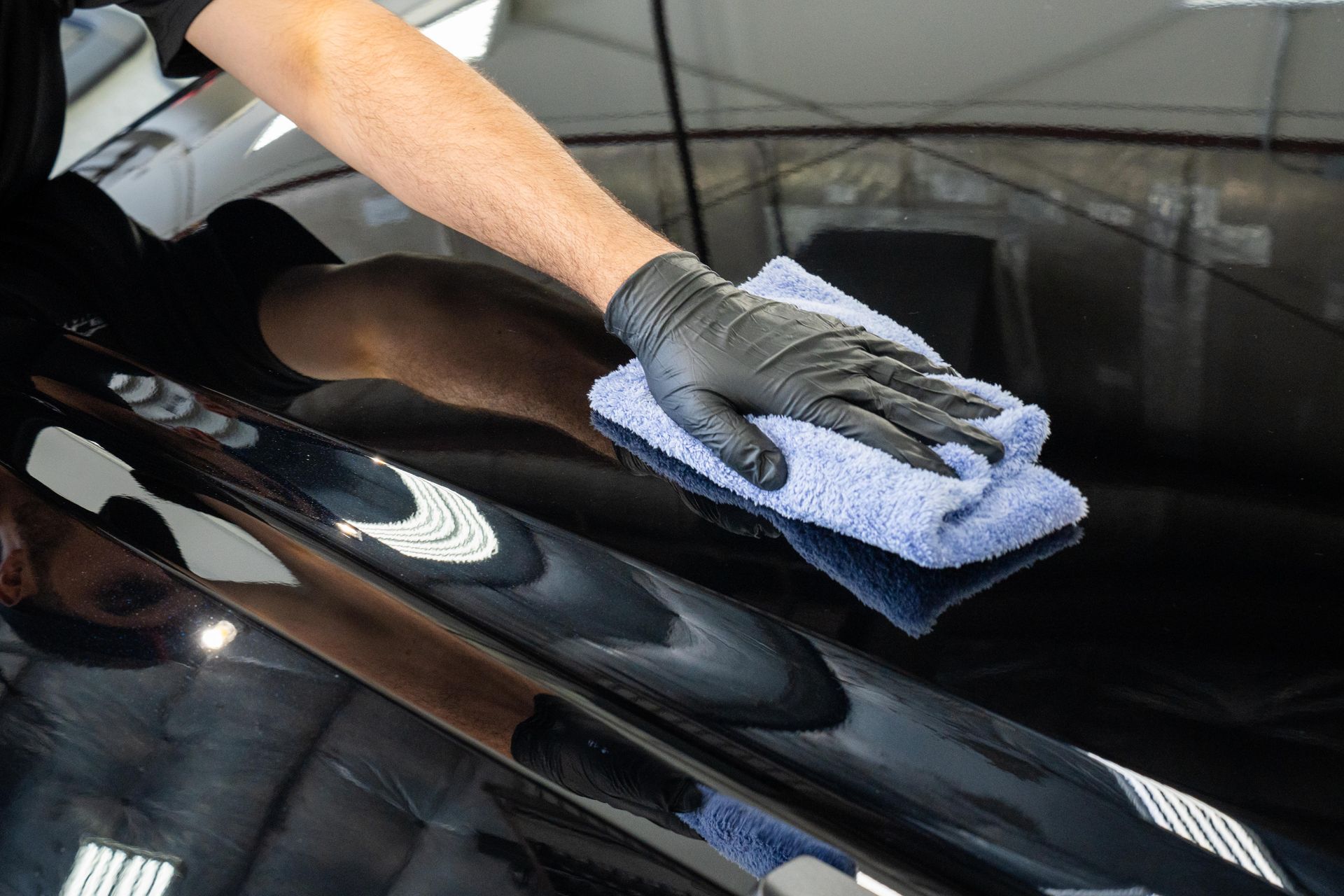 A person is cleaning a car with a towel and gloves.